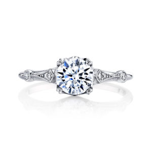 A brilliant center stone floats atop regal diamond set arches, finished with intricate milgrain detailing, in this stunning vintage inspired design from the Hera Bridal Collection.